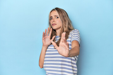 Blonde young caucasian woman in blue studio being shocked due to an imminent danger