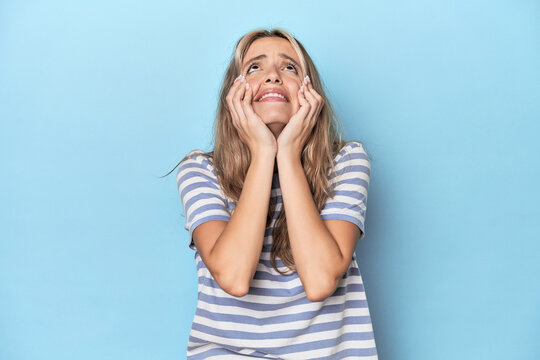 Blonde young caucasian woman in blue studio crying, unhappy with something, agony and confusion concept.