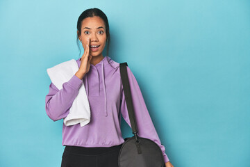 Filipina with gym gear on blue studio is saying a secret hot braking news and looking aside