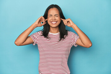 Fototapeta premium Filipina young woman on blue studio covering ears with fingers, stressed and desperate by a loudly ambient.
