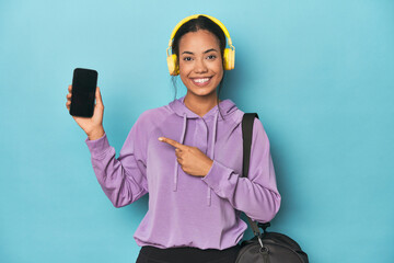 Filipina showcasing phone screen with headphones on blue backdrop