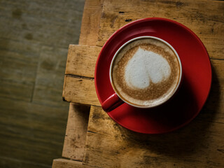 heart shaped coffee latte in a red coffee cup on the table in cafe ambience with copy space