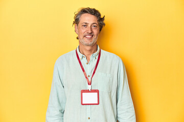 Man with an event ID card around his neck against a yellow backdrop.