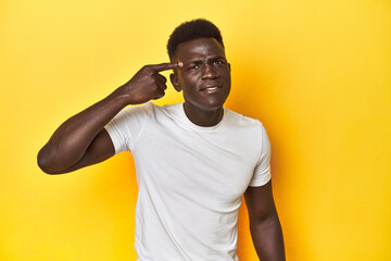 Stylish young African man on vibrant yellow studio background, showing a disappointment gesture with forefinger.