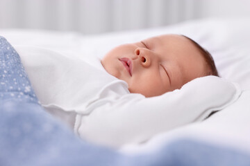 Cute newborn baby sleeping under blue blanket on bed, closeup