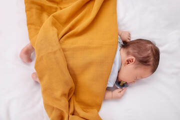 Cute newborn baby with pacifier sleeping under blanket on bed, top view