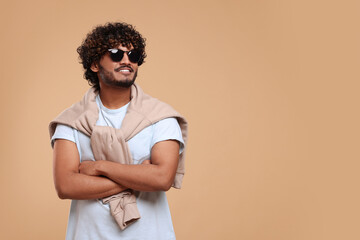 Handsome young smiling man in sunglasses on beige background, space for text