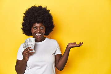 African-American woman holding cash, displaying wealth showing a copy space on a palm and holding another hand on waist.