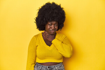 Fototapeta na wymiar African-American woman with afro, studio yellow background suffers pain in throat due a virus or infection.