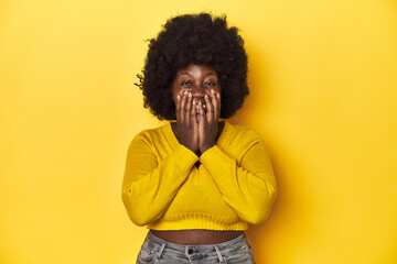 Fototapeta na wymiar African-American woman with afro, studio yellow background laughing about something, covering mouth with hands.