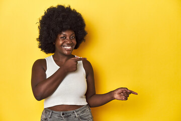 African-American woman with afro, studio yellow background pointing with forefingers to a copy...