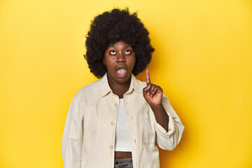 African-American woman with afro, studio yellow background having an idea, inspiration concept.