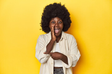 Fototapeta na wymiar African-American woman with afro, studio yellow background saying a gossip, pointing to side reporting something.