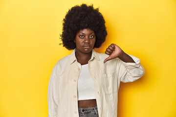 African-American woman with afro, studio yellow background showing a dislike gesture, thumbs down....