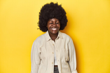 Fototapeta na wymiar African-American woman with afro, studio yellow background laughs and closes eyes, feels relaxed and happy.