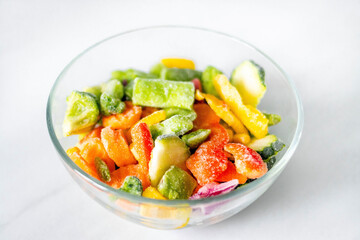 Frozen vegetables in a glass plate on a white background. The concept of healthy eating