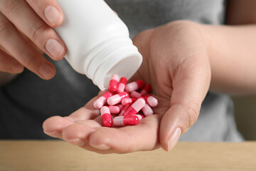 Woman pouring pills from bottle at table, closeup