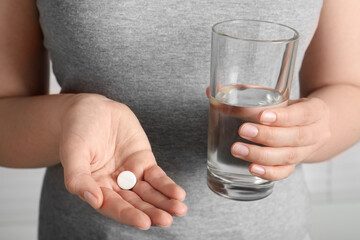Woman holding glass of water and pill, closeup