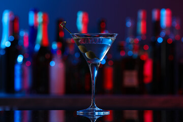 Martini glass with cocktail and olives on counter in bar