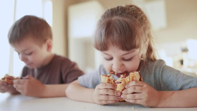 children eat burgers. fast food burger. a group of small children in the kitchen greedily eat fast food burgers. big family small kids having breakfast in the morning sun in the kitchen eating burger
