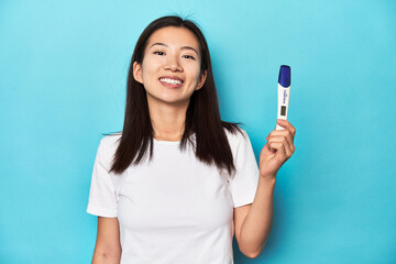 Young Asian woman holding a pregnancy test, studio shot.