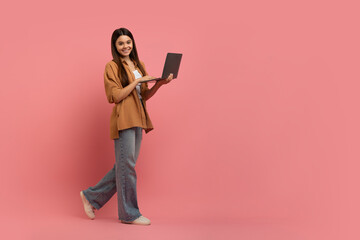 Smiling Teen Girl With Laptop Computer In Hands Walking On Pink Background