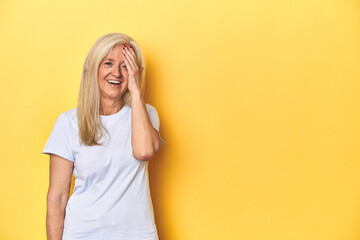 Middle-aged Caucasian woman in white t-shirt, yellow studio laughing happy, carefree, natural emotion.