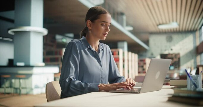 Beautiful Caucasian Female Student Working on Her School Thesis on a Laptop Computer. Young Smart Woman Sitting Behind a Desk, Studying an Online Course in an Empty Public Library with Modern Design