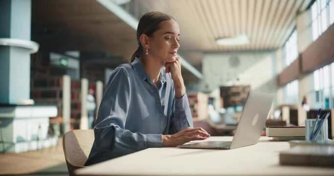 Female University Graduate Using a Laptop Computer in a Campus Reading Hall of a Modern Library with Sunlight. PhD Scholar Making a STEM Research Project with Focus on Science and Engineering