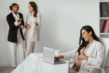 Businesswomen pointing at pregnant woman working on laptop in office, worker harassment and discrimination - obrazy, fototapety, plakaty