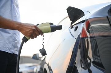 Serious african man holding charge cable in on hand, standing near luxury electric car.