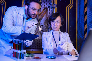 indian scientist pointing with pan at samples near colleague in futuristic scientific laboratory