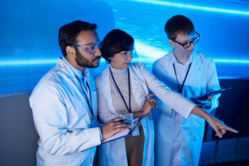 futuristic science center, woman scientist pointing with finger near multiethnic colleagues