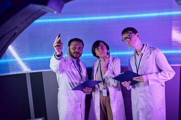 indian scientist pointing with pen at new device near colleagues in futuristic discovery center