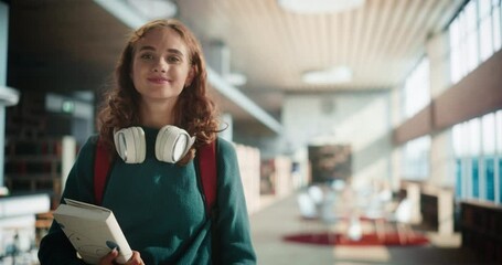 Beautiful Caucasian STEM Student Standing in a Modern Library of Her University with an Academic textbook. Young Happy Successful Woman Looking at Camera, Smiling. Education and Learning Concept