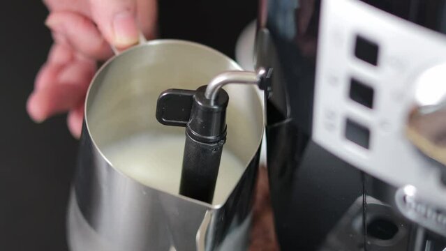 A man froths milk in a metal mug with a cappuccinatore in a coffee maker. Close-up of a mug with milk. Morning coffee.