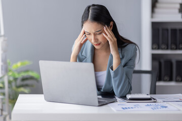 Portrait of tired young business Asian woman work with documents tax laptop computer in office. Sad, unhappy, Worried, Depression, or employee life stress concept
