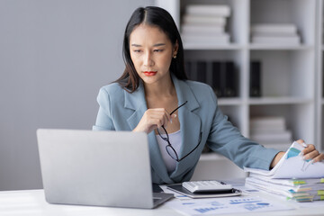 Portrait of tired young business Asian woman work with documents tax laptop computer in office. Sad, unhappy, Worried, Depression, or employee life stress concept
