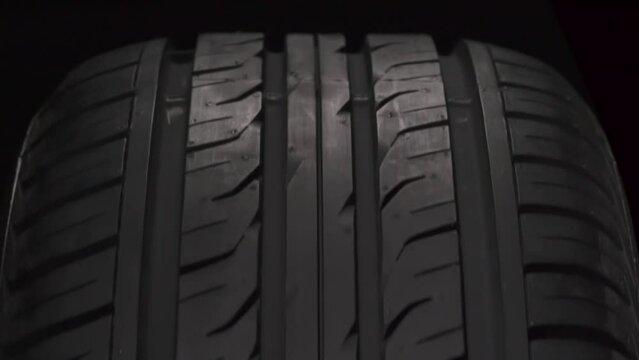 Fast Spinning Car Wheel. The new car tire is highlighted by a spotlight in the dark. The wheel rotates slowly toward the viewer against a black background