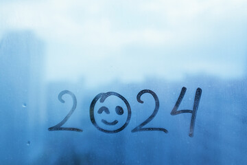 Handwritten blue arabic numerals 2024 doodle smiling face winks on misted glass on window flooded...