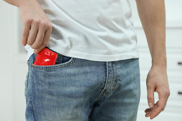 Man pulling condom out of pocket indoors, closeup