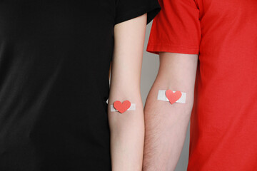 Blood donation concept. Couple with adhesive plasters on arms against grey background, closeup