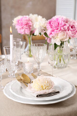 Stylish table setting with beautiful peonies and burning candle indoors