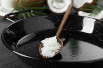 Frying pan with organic coconut cooking oil and wooden spoon on grey table, closeup