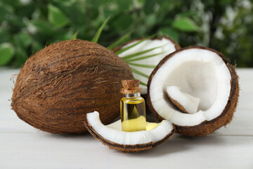Fototapeta na wymiar Bottle of organic coconut cooking oil, leaf and fresh fruits on white wooden table, closeup
