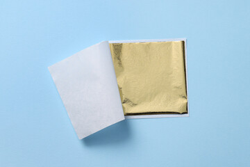 Edible gold leaf sheet on light blue background, top view