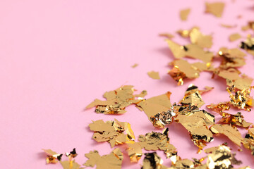 Many pieces of edible gold leaf on pink background, closeup. Space for text