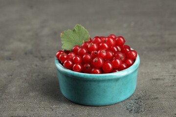 Ripe red currants and leaf in bowl on dark textured table, closeup