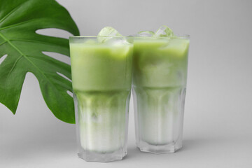 Glasses of tasty iced matcha latte and leaf on light grey background