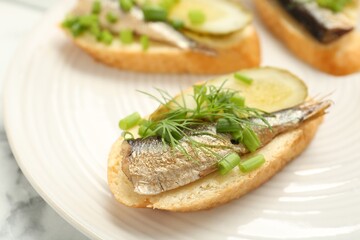 Delicious sandwiches with sprats, pickled cucumber, green onion and dill on plate, closeup